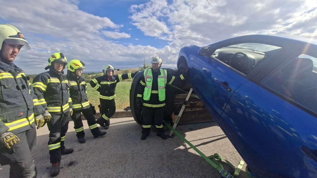Feuerwehrleute sichern ein auf der Seite liegendes blaues Auto auf einer Straße im Burgenland.