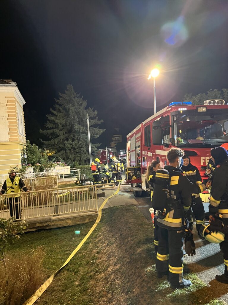 Feuerwehrleute im Einsatz mit Löschfahrzeug und Schlauch bei Nacht in einem Wohngebiet